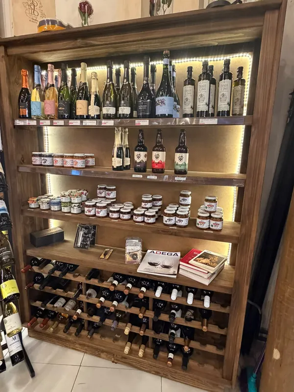 Estante iluminada com espumantes, vinhos, conservas e livros sobre vinho