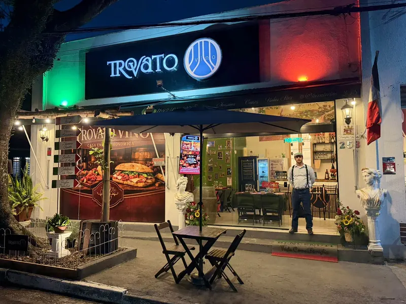 Fachada da Trovato Vino à noite, com o letreiro aceso, luzes verde e vermelha, mesa na calçada e o Júlio na porta