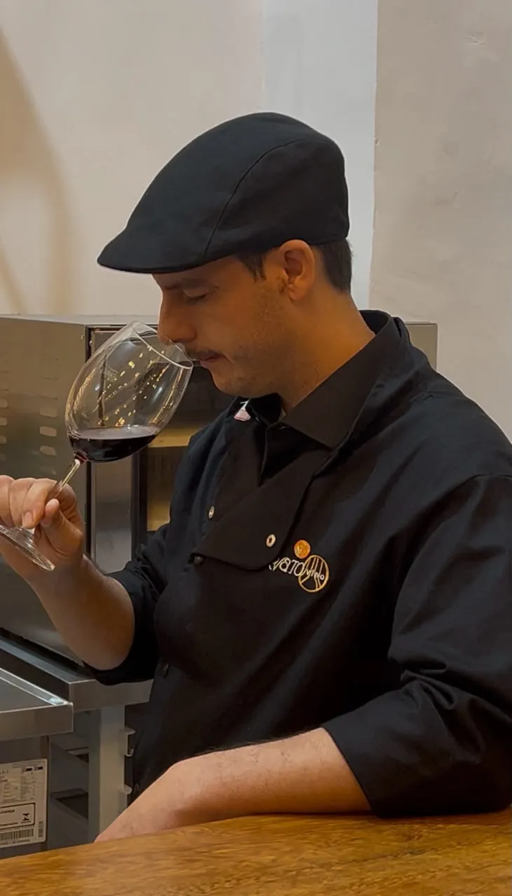 Júlio Trovato, de boina e dólmã com o logo da casa, sente o aroma de uma taça de vinho tinto no balcão