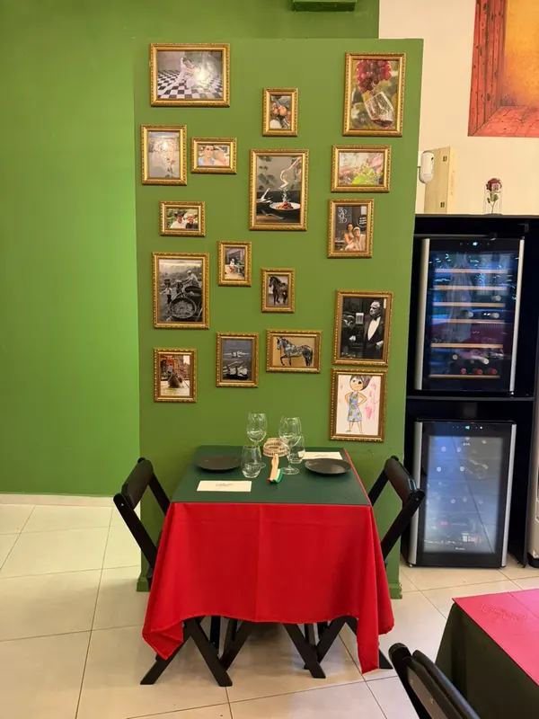 Mesa para dois diante de uma parede verde com quadros de moldura dourada, ao lado das adegas climatizadas