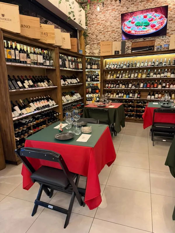 Salão com mesas de toalha vermelha e verde entre estantes de madeira cheias de vinho